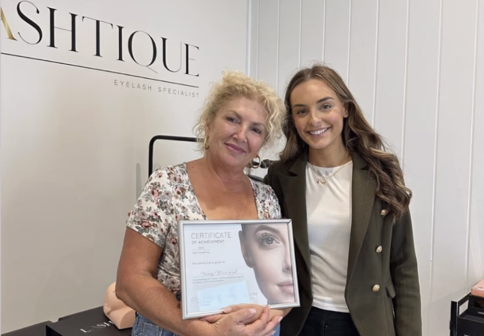Trainer and students holding framed lash certification diplomas in beauty studio setting.