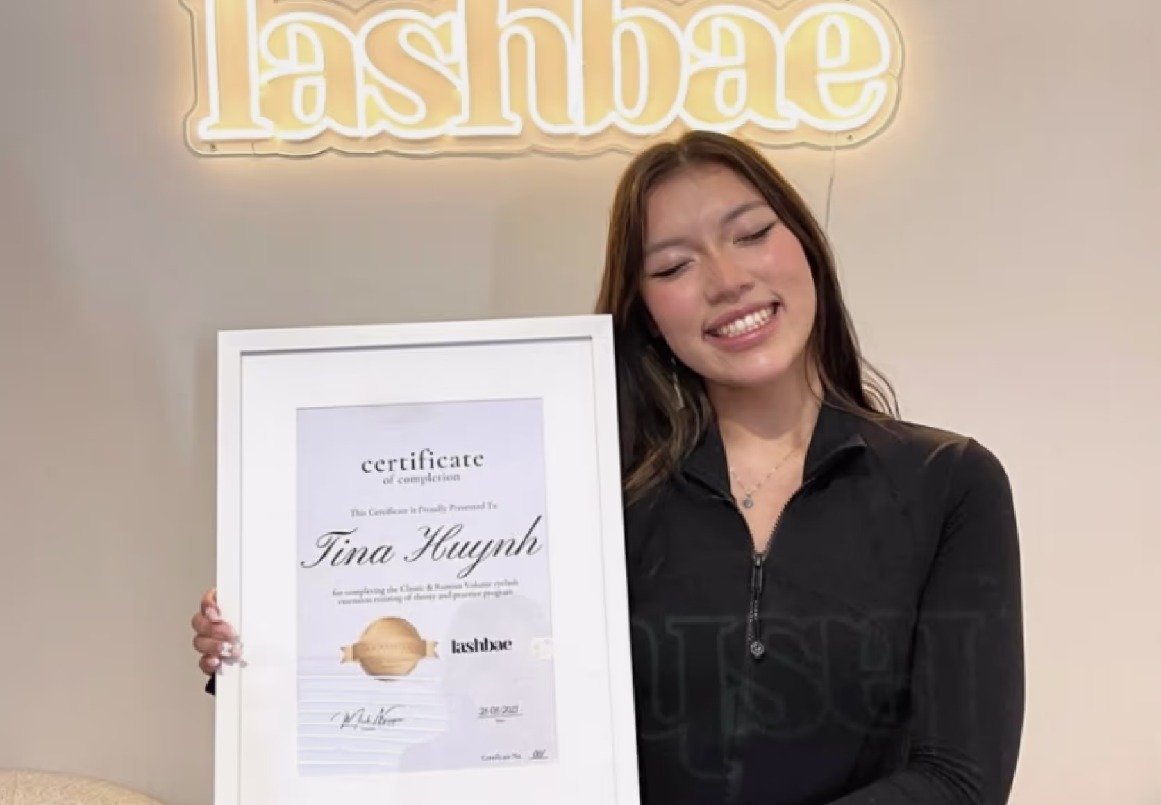 Students holding framed lash certification diplomas in beauty studio setting.