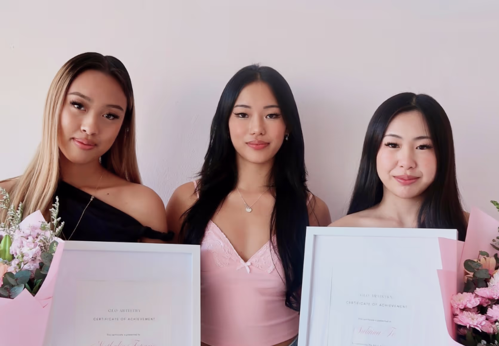 Trainer and students holding framed lash certification diplomas in beauty studio setting.