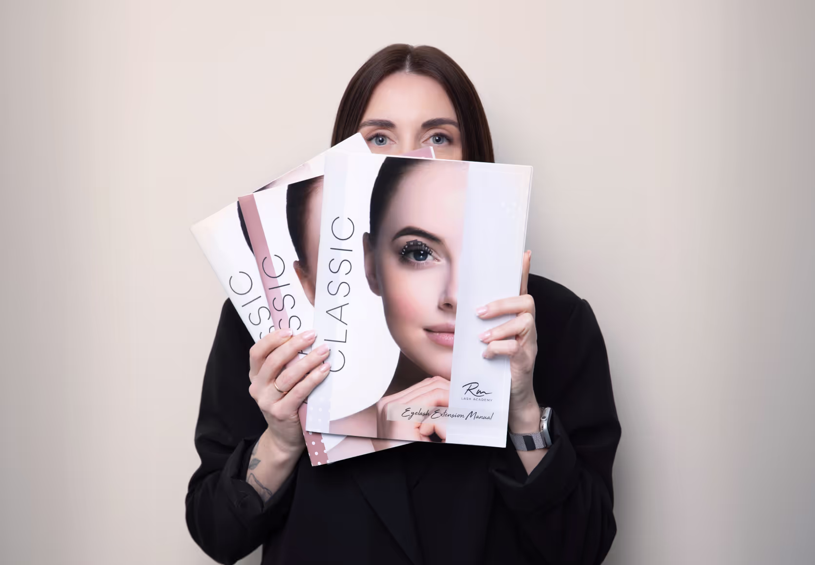 Woman holding RM Lash Academy training booklets in front of her face.