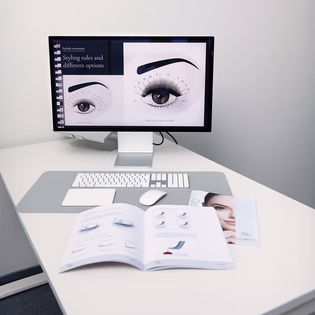 Lash training station with computer screen and printed manual showing lash styling techniques and diagrams.