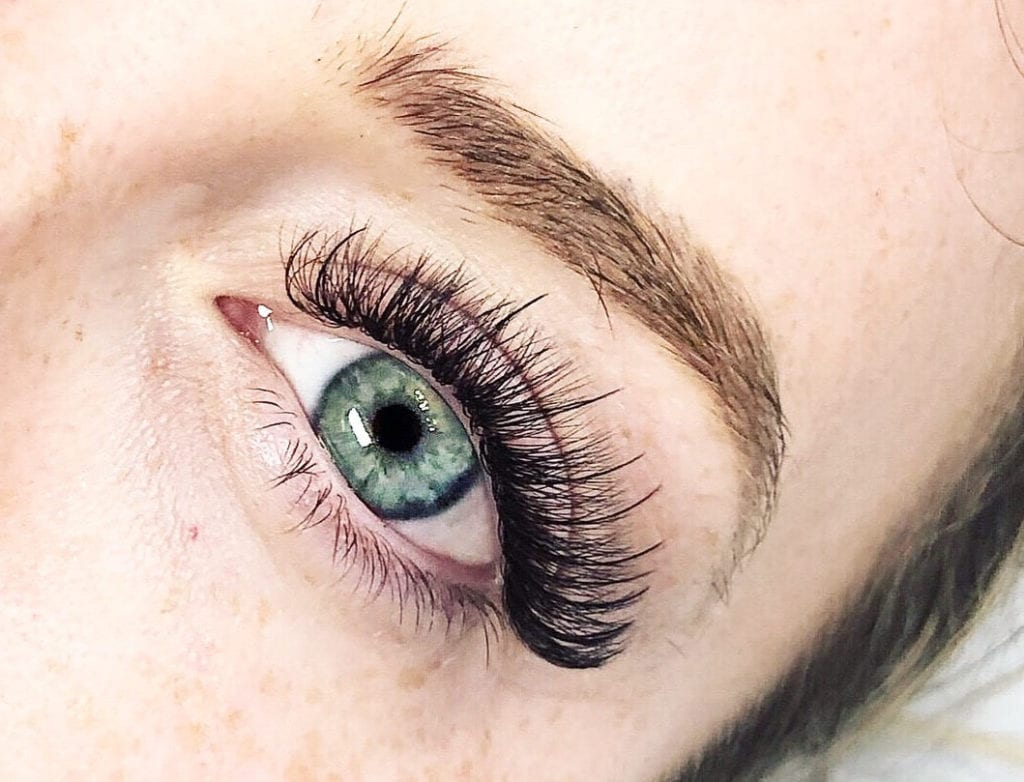 Close-up of a woman’s eye with hybrid eyelash extensions, showing a mix of classic and volume lashes for a natural yet voluminous look, with wispy lashes framing the eye.