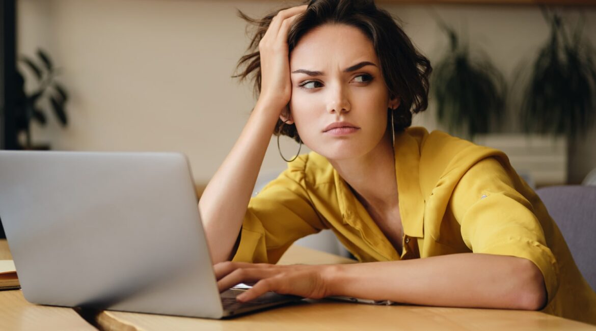A woman sitting at a desk with a worried expression, contemplating the five mistakes made when starting a lash extension business.