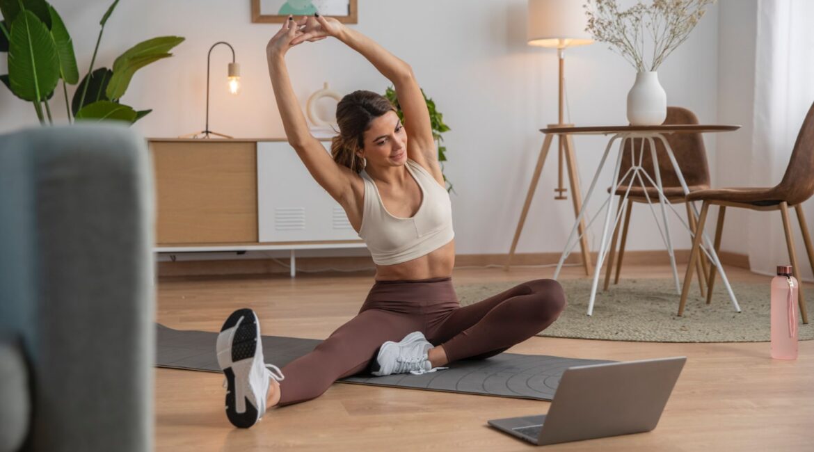 Woman stretching her back on a yoga mat in front of an open laptop.