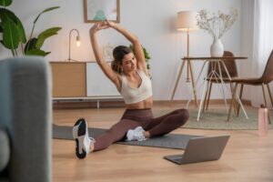 Woman stretching her back on a yoga mat in front of an open laptop.