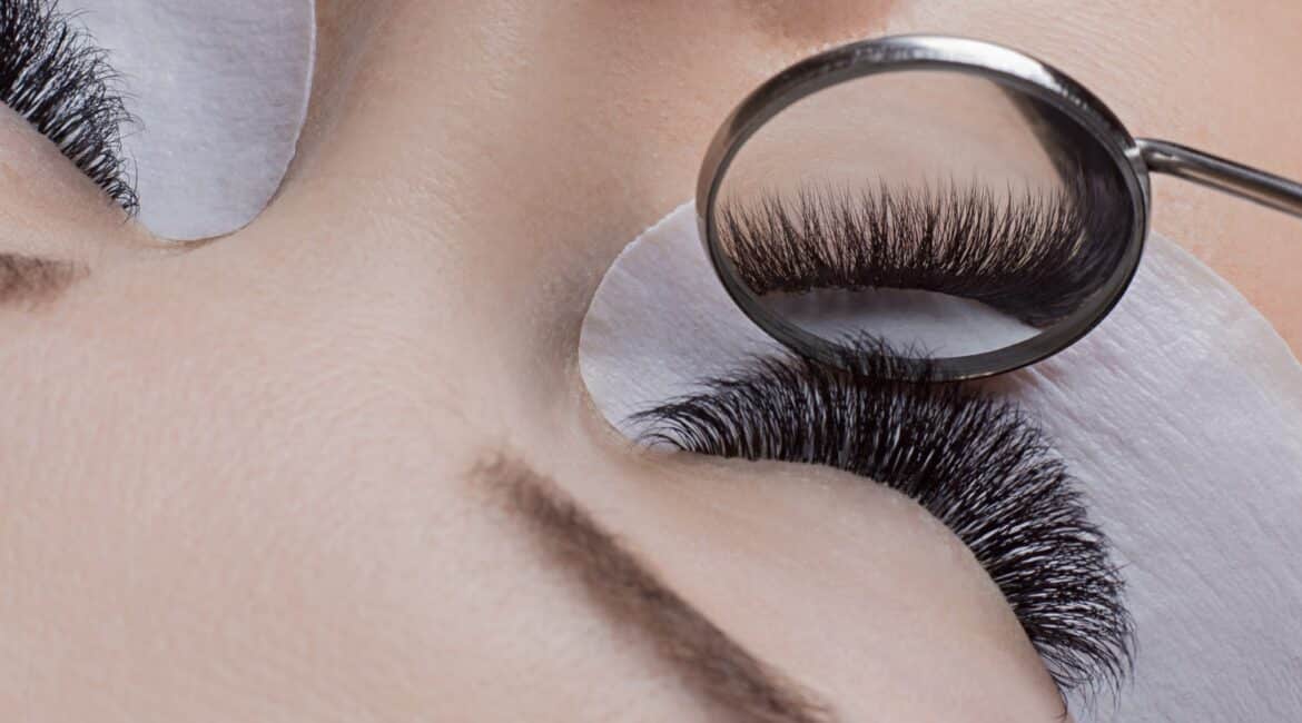 Technician inspecting volume lashes with a small oval mirror, revealing meticulous lash application.
