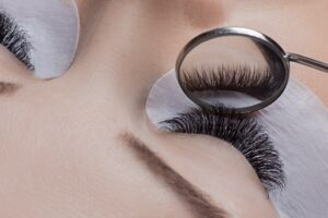 Technician inspecting volume lashes with a small oval mirror, revealing meticulous lash application.